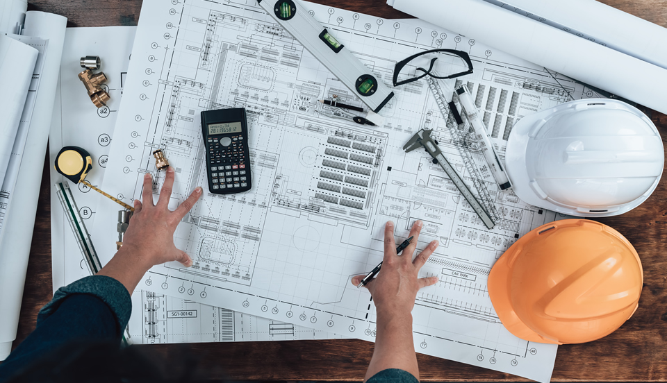 calculator, ballpens, blueprint, level bar, roll meter, ruler, and goggles laid on top of a blueprint